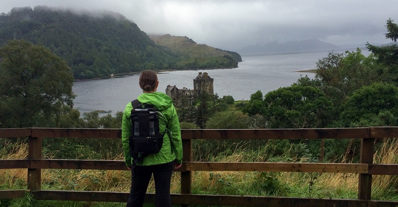 Woman standing with a portable oxygen concentrator on her back looking at a castle in Scotland