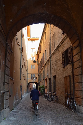 A man biking under an arch in a small street in Ferrara, Italy