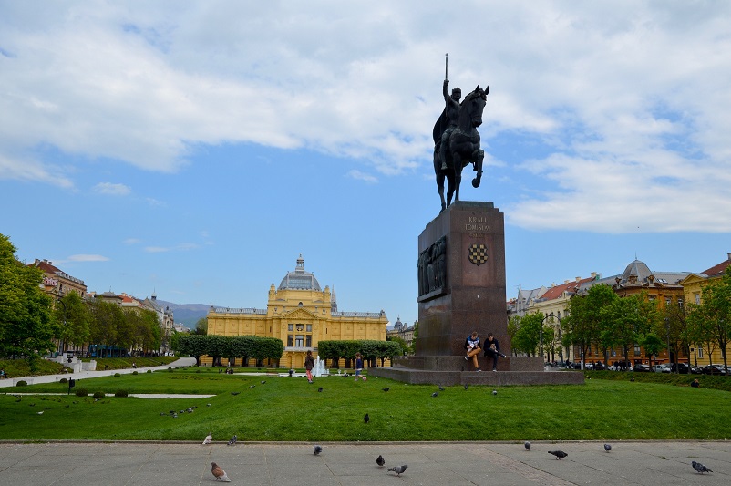 Statue of a man on a horse and big yellow building in Ledeni Park in Zagreb, Croatia