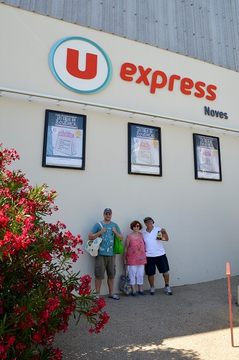 Three people holding groceries outside a U Express in Noves, France