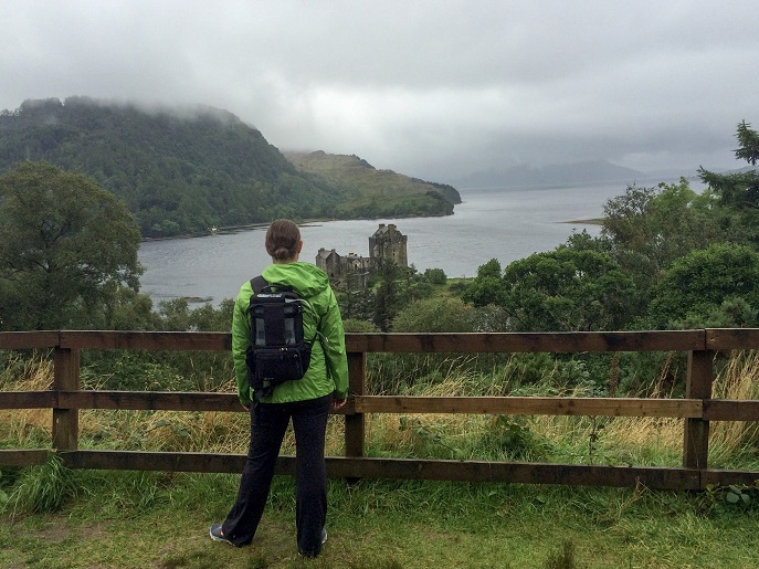 Woman standing facing a foggy, grey scene in Scotland while wearing a portable oxygen concentrator on her back