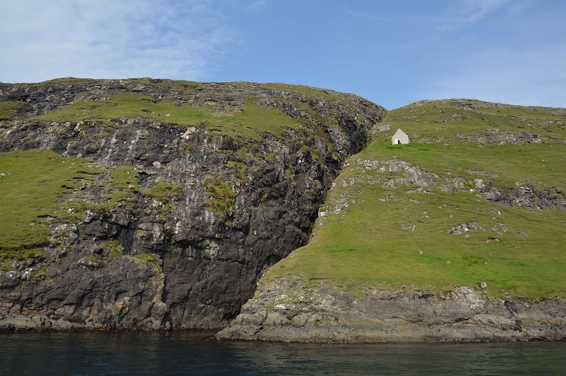 A small white house sitting on green cliffs in the Faroe Islands