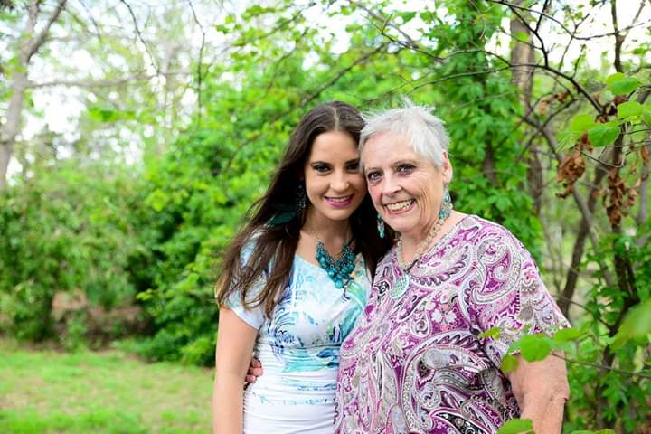 Two smiling women - mother and daughter - in front of green trees 