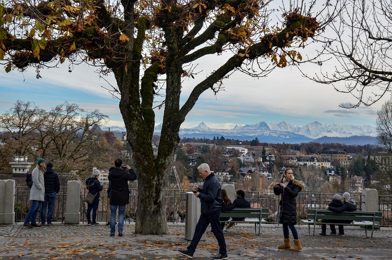 People walking in front of and taking pictures of the Swiss alps in Bern, Switzerland