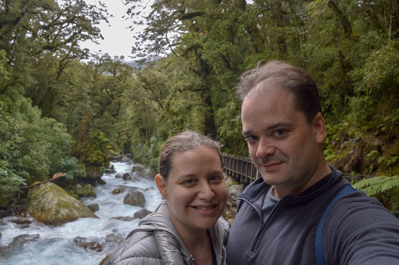 Man and woman smiling in front of rushing water on the Lake Marian Track in New Zealand