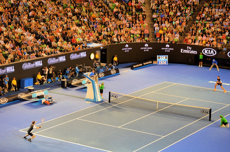 Two men playing tennis indoors with a massive crowd at the Australian Open
