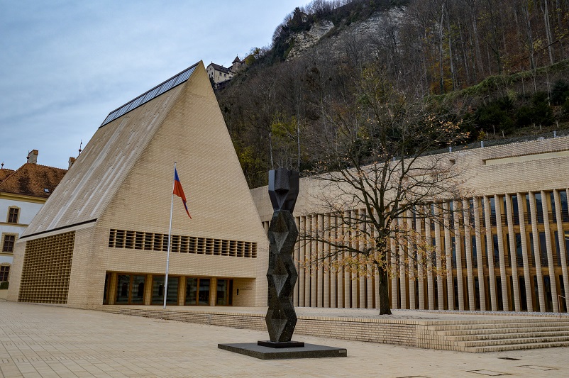 A statue, tree, and flag in front of the Vaduz Landtag building, one of the things to do in Vaduz