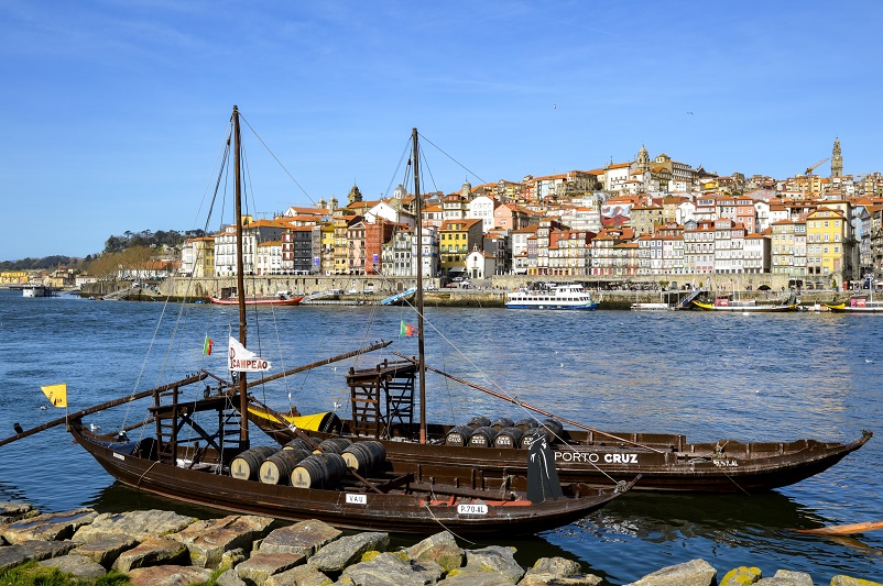 Two small Port boats on a bright blue river with a picturesque view of colorful houses behind in Porto, Portugal