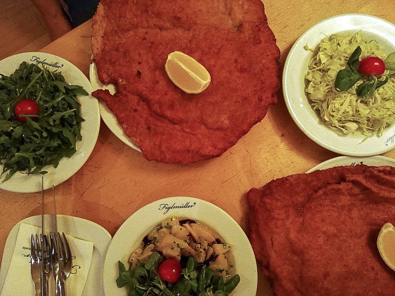Two schnitzels and three side dishes on a table at Figlmueller in Vienna, Austria