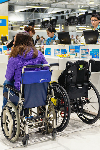 Melanie sitting in an airport wheelchair next to her own wheelchair in Narita, Japan