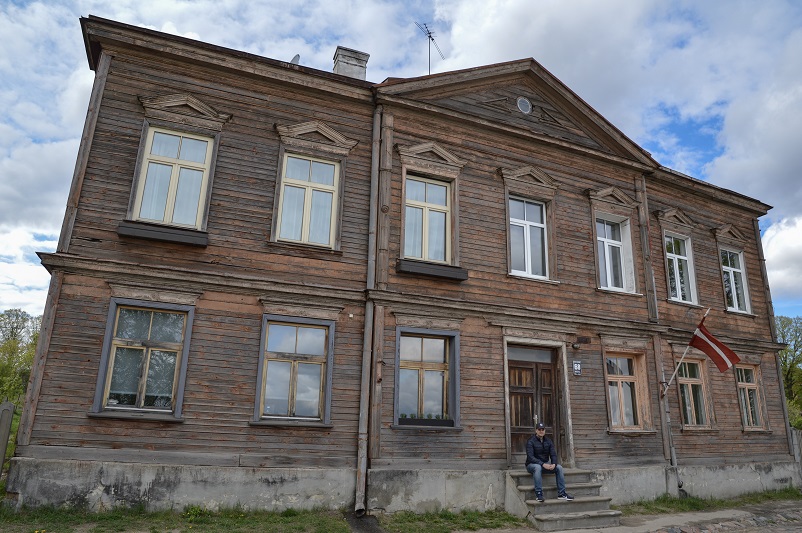 Justin sitting in front of a wooden house on Kipsala island in Riga