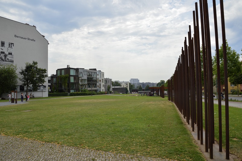 Steel rods where the Berlin wall once stood on the right; a building that says "Bernauer Strasse" on the left