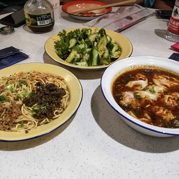 Three dishes of food on a table - noodles, cucumbers, and dumplings - on a Shanghai food tour