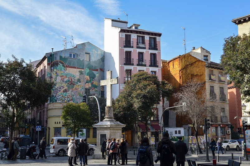 A large cross in front of three colorful buildings in Madrid