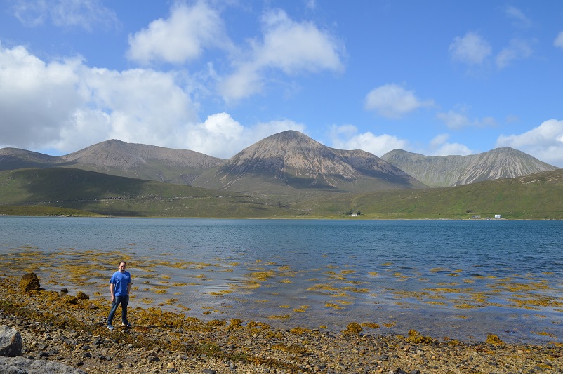 Justin standing at the edge of the water in front of mountains on the Isle of Skye in Scotland