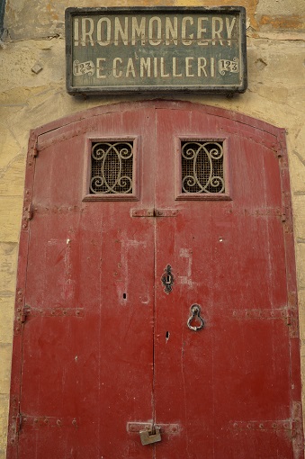 Red door in Valletta with sign above it reading "Ironmongery E Camilleri"