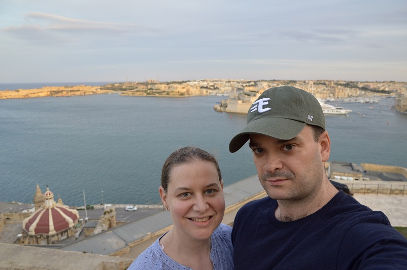 Sarah and Justin smiling with a view of the Three Cities behind them, taken at Upper Barrakka Gardens in Valletta