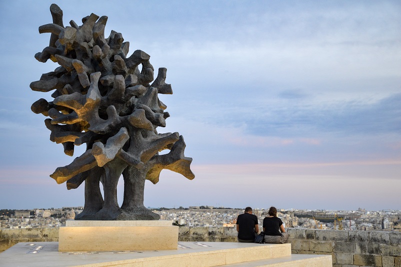 Two people sitting to the right of a large sculpture at one of our favorite Valletta photo spots