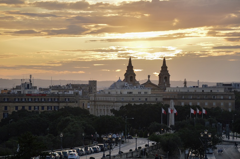 Church in the distance with Malta flags in front of it, at sunset in Valletta