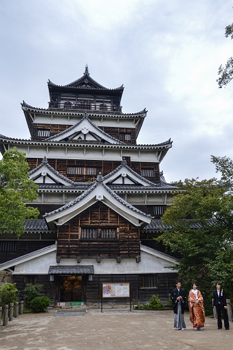 Three people walking in front of Hiroshima Castle tower