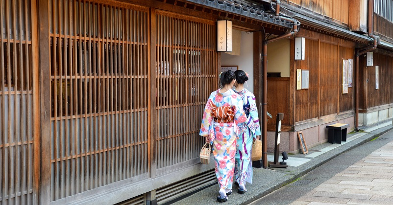 Two women in kimonos walking next to wooden building in Kanazawa, Japan