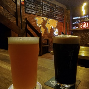 Two pints of beer in front of a tap list at Biała Małpa, where you can drink craft beer in Katowice
