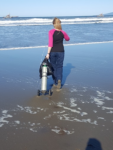 Woman walking towards the ocean rolling an oxygen canister on the beach