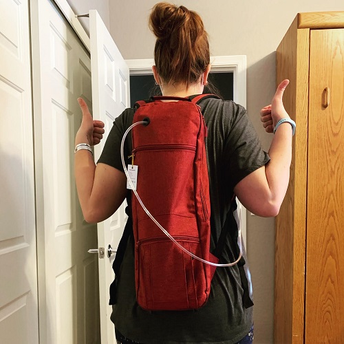 Woman with red backpack with oxygen hose sticking out giving thumbs up, as seen from behind