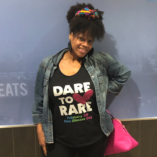 Najah, a woman wearing a "Dare to Rare" shirt and a big smile