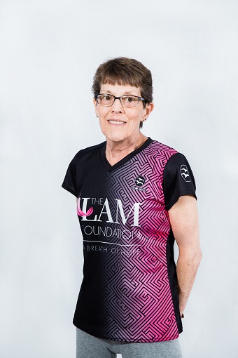 Sally, a woman in a shirt that says "LAM" standing with hands behind her back and smiling