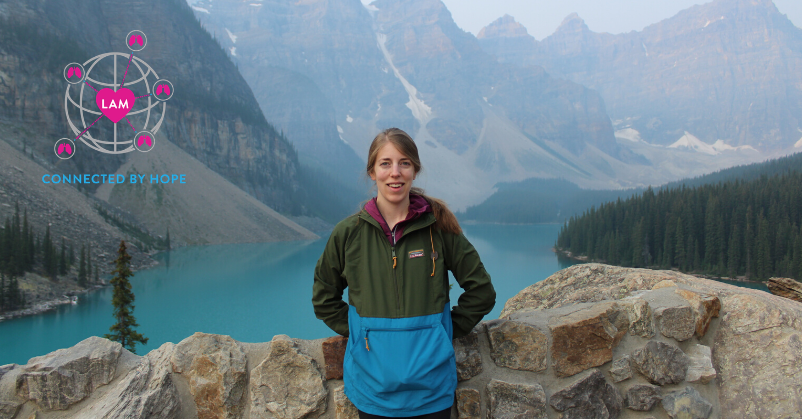 Shea, a woman, standing in front of beautiful mountains; WWLAM logo in top right corner