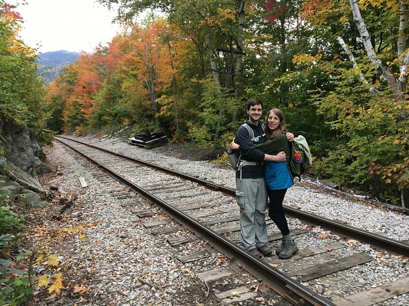 Shea and her husband standing on train tracks in the woods in New Hampshire