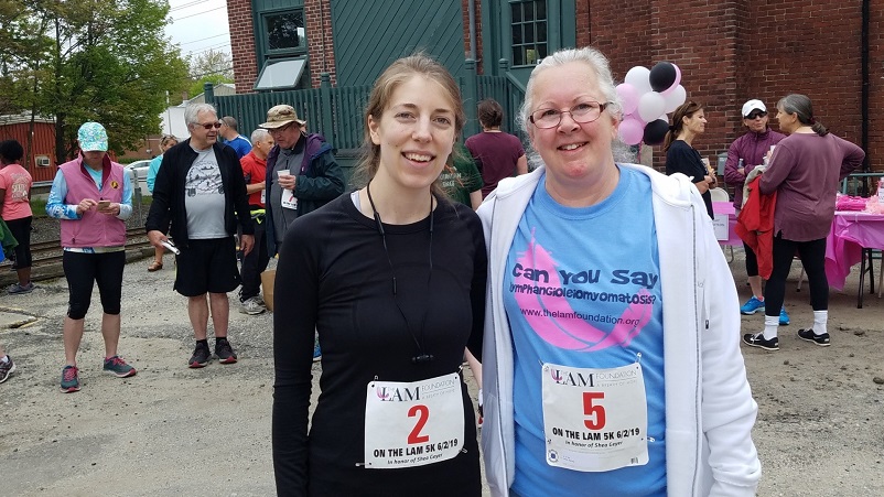 Shea and her mom with running bibs; her mom is wearing a shirt that says "can you say lymphangioleiomyomatosis?"