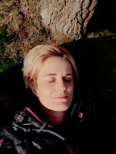 Sina (a woman with short blonde hair) lying on a rocky terrain with her eyes closed