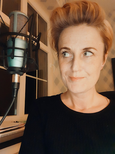 A woman with short blonde hair looking cheekily over at the microphone next to her face