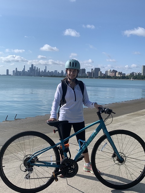 Alex standing with her bike and oxygen in front of water and a city skyline