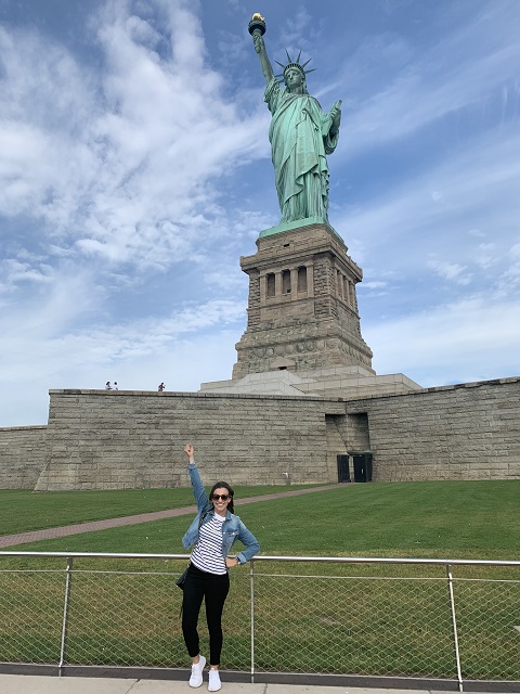 Alex, a woman with LAM, standing with her arm raised in front of Lady Liberty