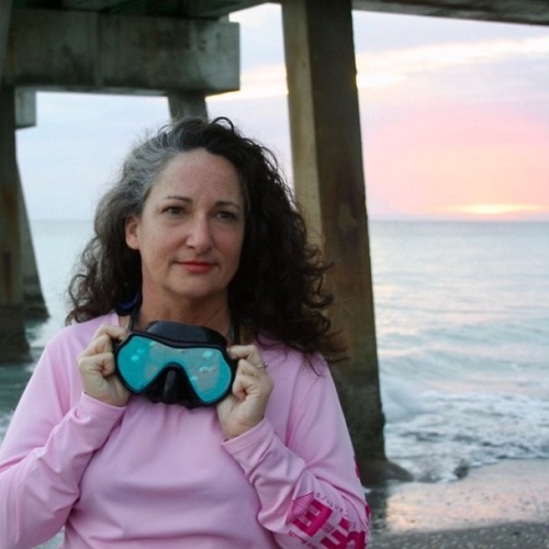 Headshot of a woman with googles standing in front of the ocean