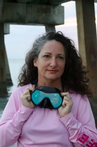 Sarah, a woman with LAM, holding scuba goggles standing in front of the ocean